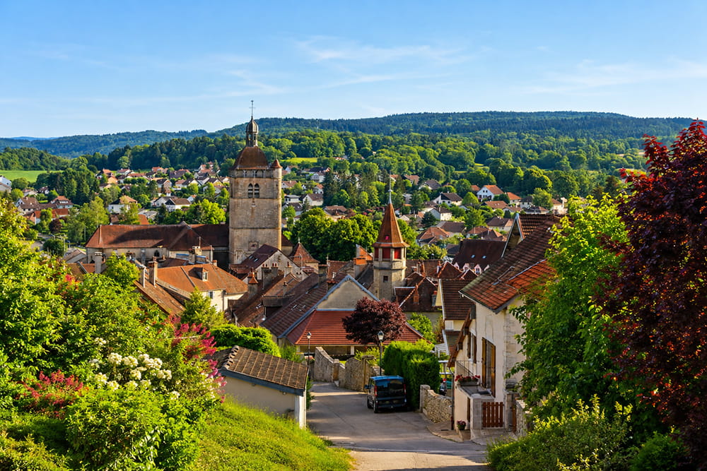 Vue panoramique sur Orgelet, son église et les toits du village entourés par les paysages verdoyants du Jura.